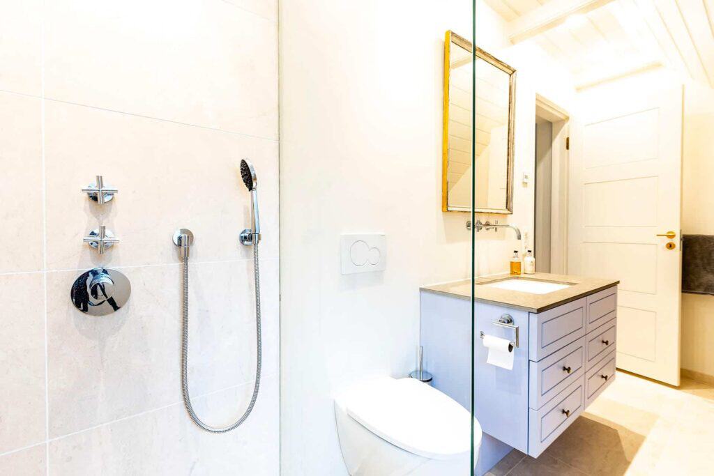 Brusekabine med glasvægge, med toilet og håndvask i baggrunden (med tilslutning af jordvarmepumper)