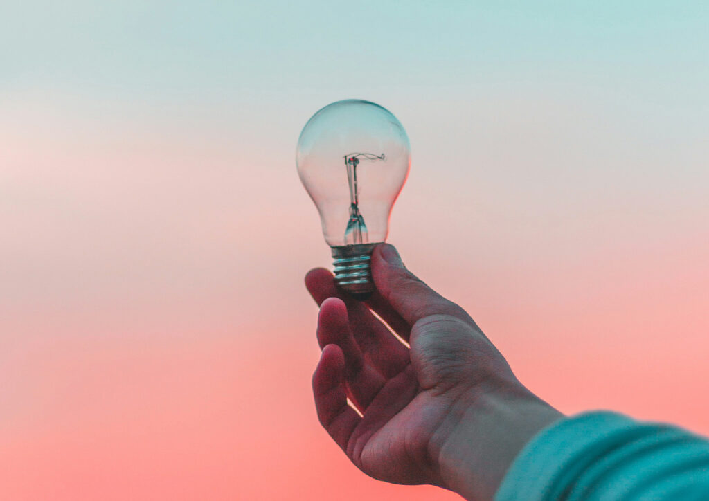 Hand holding a lightbulb with soft sunset colors in the background.