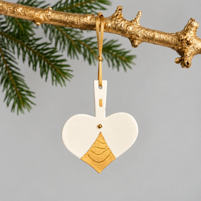Keramisk julehjerte ornament med gulddetaljer hængende på gren.