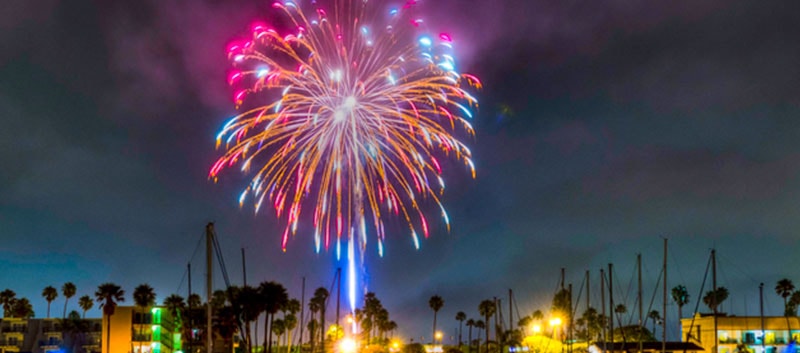 A firework explodes; bright purple, blue and red light streams from the night sky