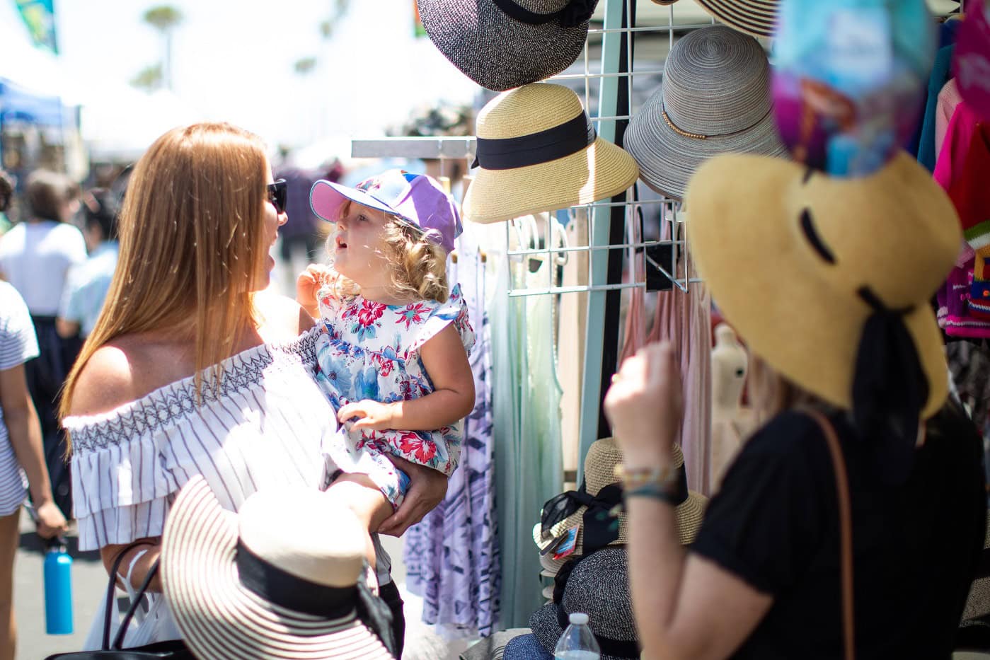 Happy toddler trying on hats with Mom at the Farmers' Market