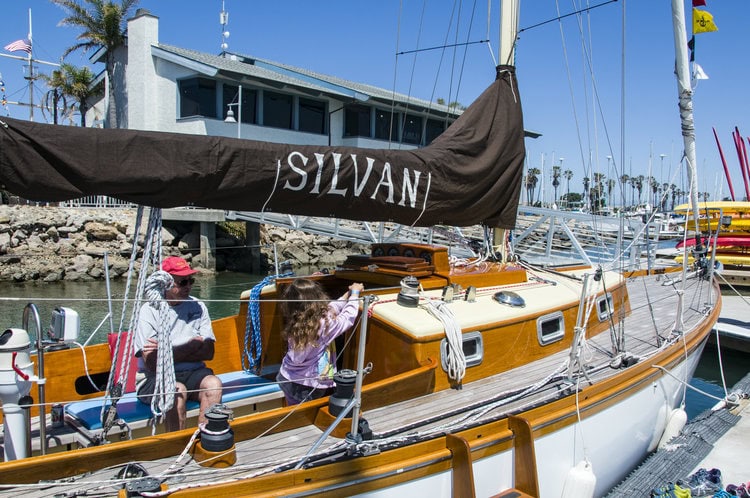 A classic wooden boat anchored in the harbor, white with chrome and laqueryed wooden trim, weather worn deck