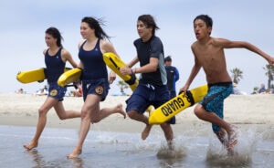 Group of young lifeguards running into the water with rescue paddles at Channel Islands Harbor.