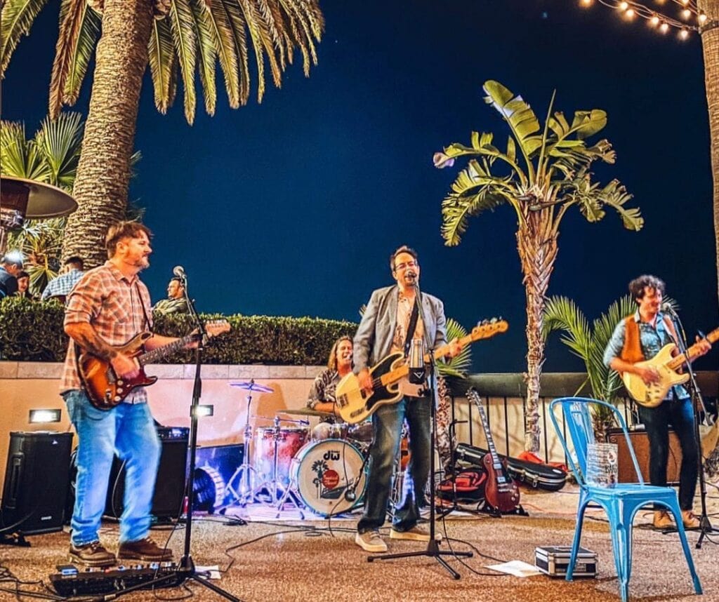 Live band playing music outdoors at Channel Islands Harbor with palm trees at night.