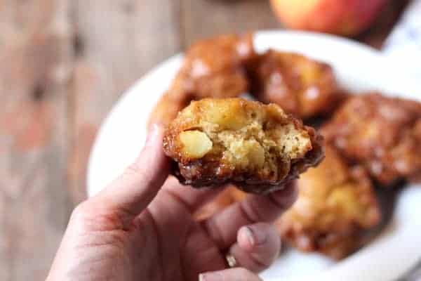 Photo shows a hand holding an apple fritter with a bite taken out of it