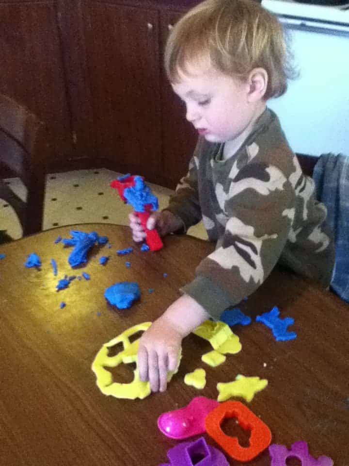 Image shows a little boy in a camouflage sweatshirt standing at a table playing with blue play dough