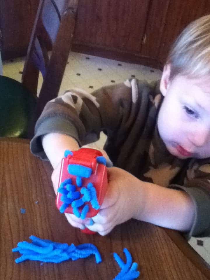 Image shows a little boy playing with a Play-Doh toy and blue dough over a table.