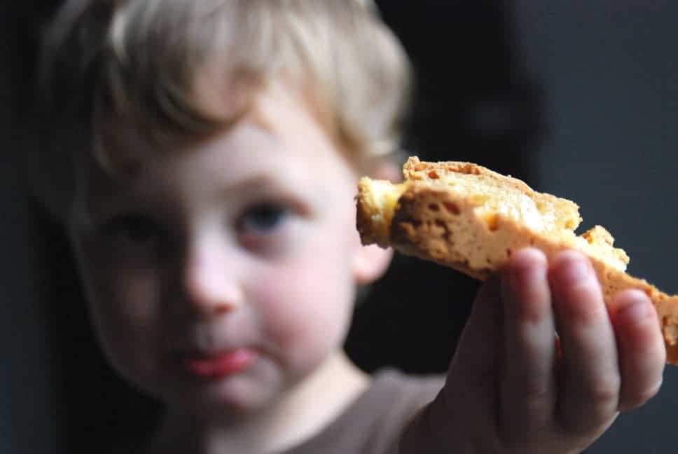 Image shows a young boy holding a piece of gluten free bread. The bread is in the foreground, and the boy is blurred in the background.