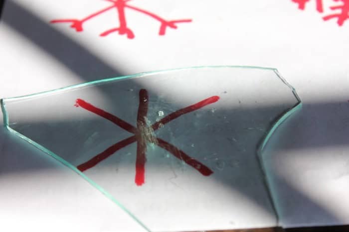 Image shows a close up of a piece of glass on white paper with a red snowflake drawn