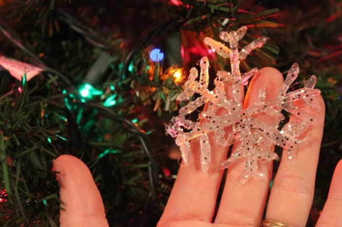 Photo shows a hand behind a snowflake ornament in a tree