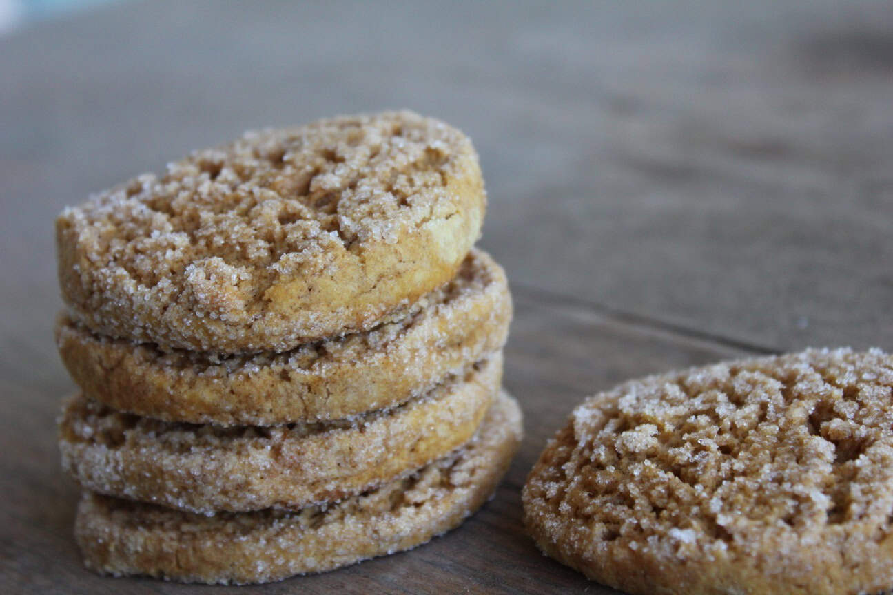 Image shows a stack of gluten free sweet potato cookies covered in sugar, stacked on a table. A single cookie sits next to the stack on the table. 