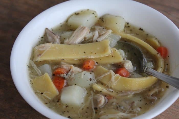A heaping bowl of gluten free chicken noodle soup sits on a table