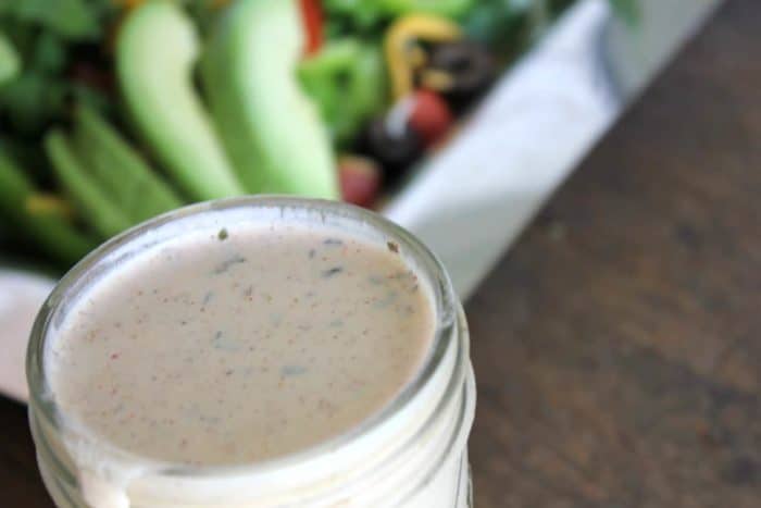 Image shows a jar of dressing in front of a green salad