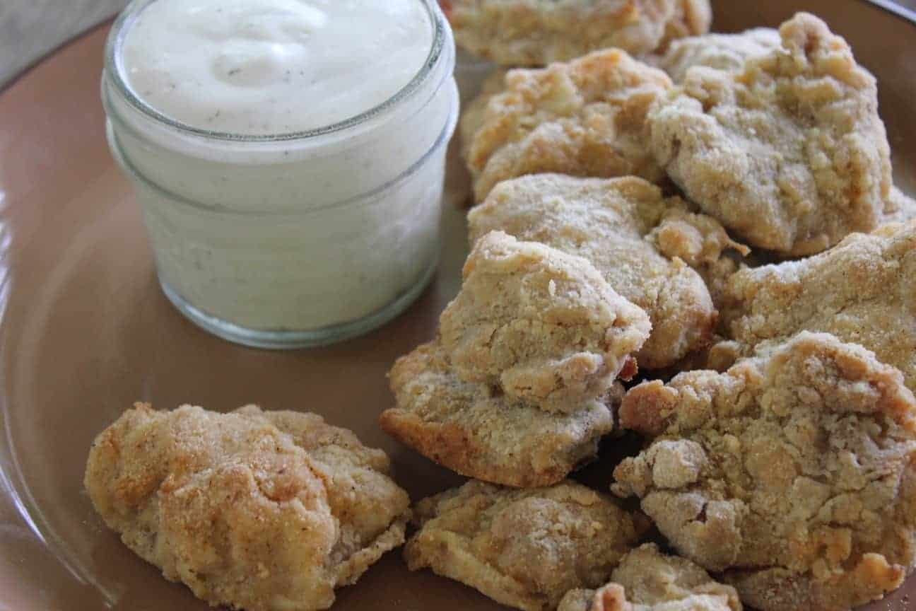 Image shows a pile of homemade gluten free chicken nuggets on a glass dish with a small jar of ranch dressing next to them.