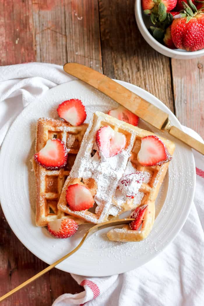 gluten free waffles with powdered sugar and strawberries on a plate.