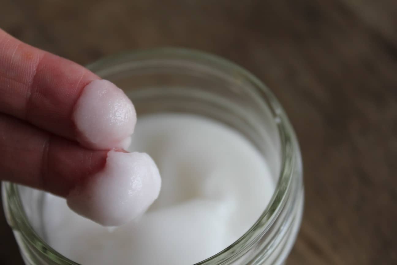 Image shows a small jar of face wash, with two fingers above the jar with the baking soda face wash on the tips. 