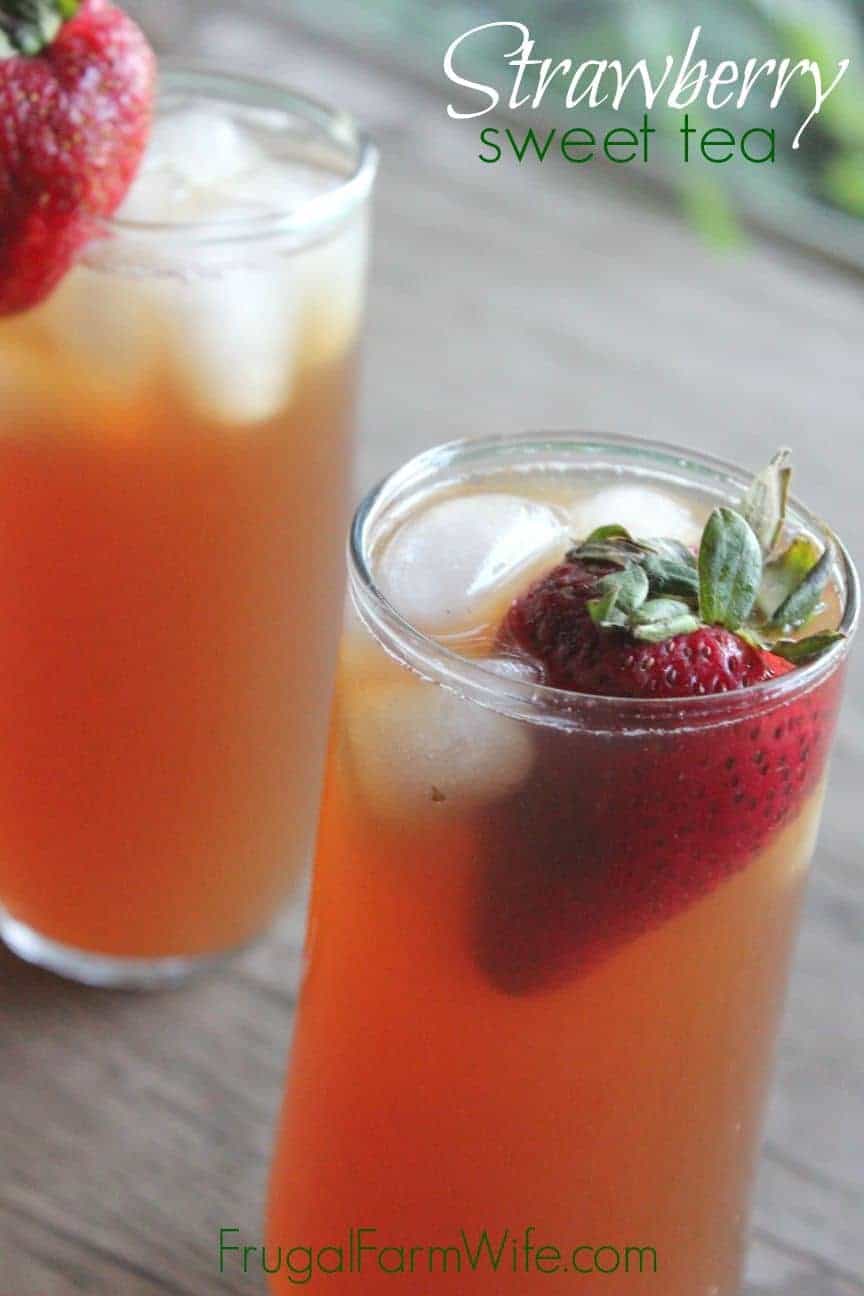 Image shows a close up of two glasses of iced tea with a strawberry floating in each. The glasses sit on a table, and text overlay reads "Strawberry Sweet Tea"