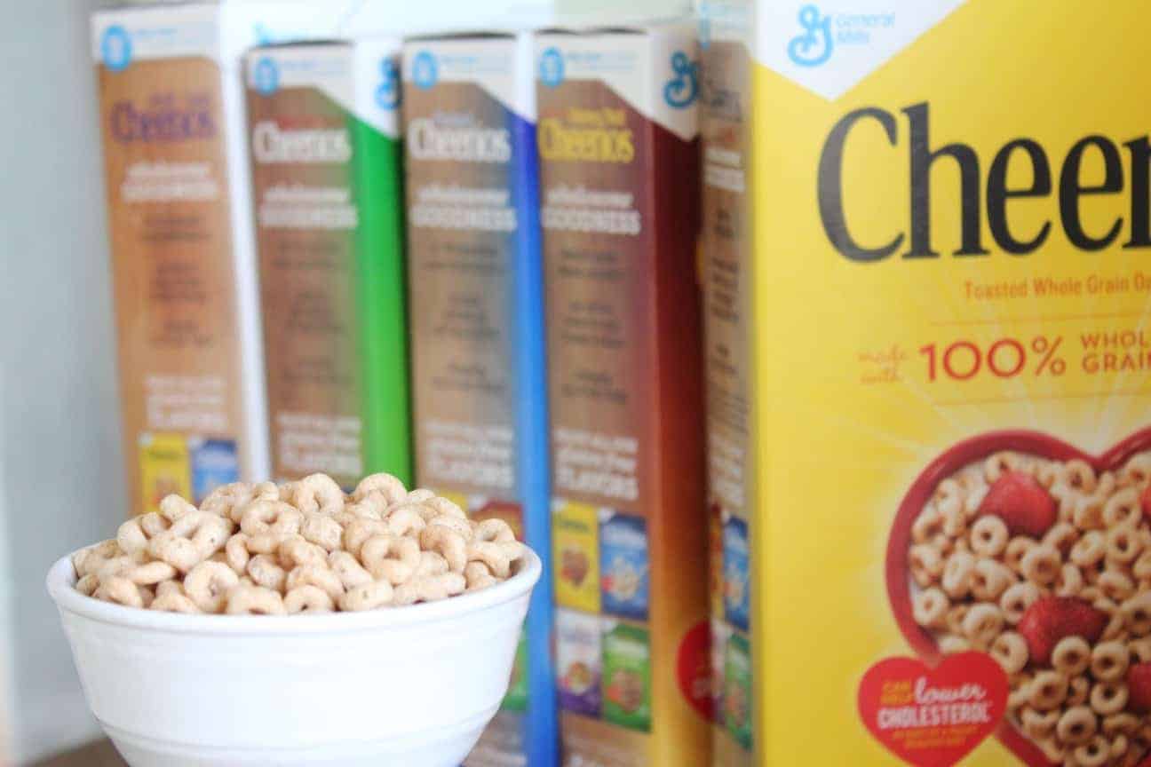 Image shows a white bowl full of Cheerios sitting on a table with boxes of the cereal.