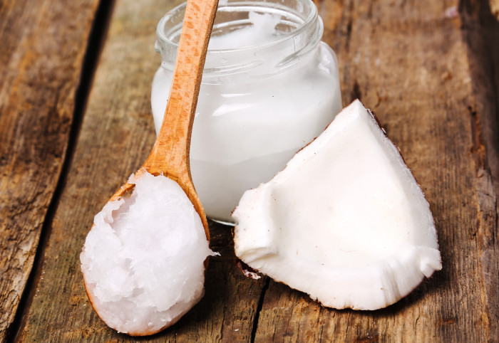 Image shows a spoon full of coconut oil next to a jar on a table