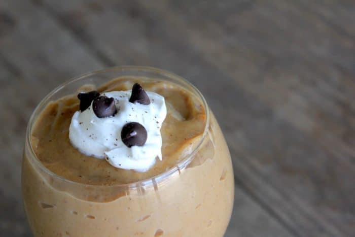 Image depicts homemade pumpkin pudding in a glass garnished with whipped cream and chocolate chips