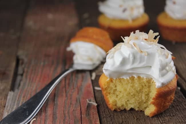 Image shows a yellow cupcake with white frosting, with a bite taken from it with a fork