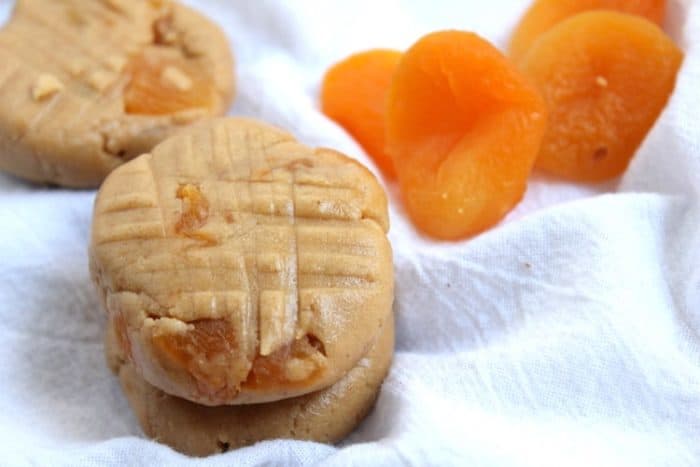 Image shows a couple of apricot cookies on a white towel next to several apricots