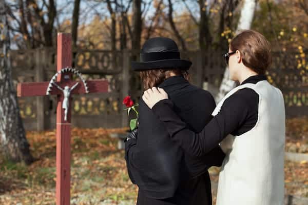 Image shows two women outside stading in front of a cross. One is comforting the other with an arm around her shoulder.