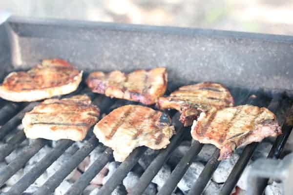 Image shows several pieces of pork cooking on the grill.