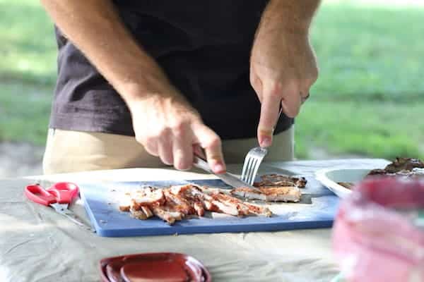 Image shows a man slicing pork with a fork and knife on a cutting board.