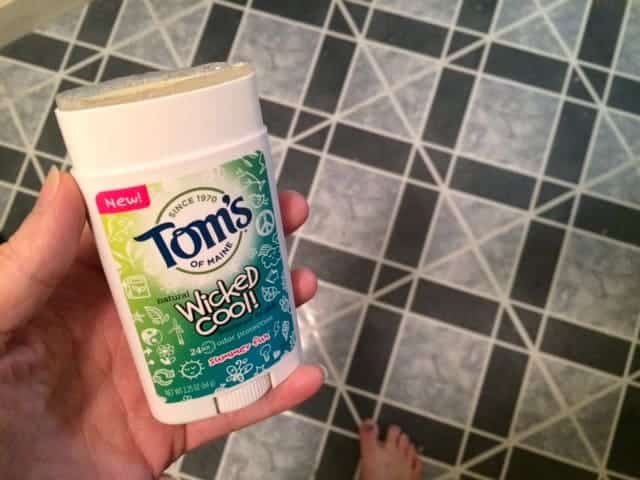 Image shows a woman's hand holding a Tom's of Maine Wicked Cool deodorant over a bathroom floor. 