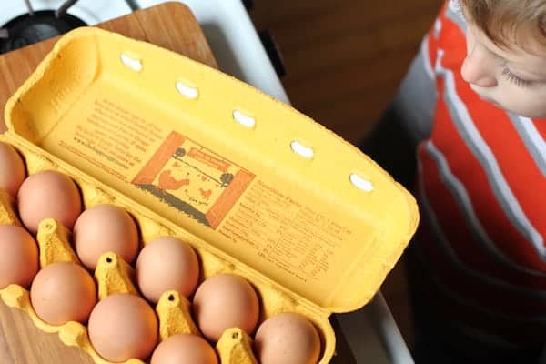 Image shows an open yellow egg carton with a dozen eggs, and a little boy looking at them