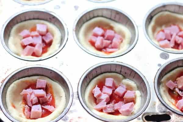 Image shows a muffin tin where the mini pizzas are being assembled