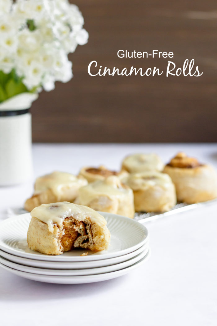 Photo shows a cinnamon roll with a bite taken out of it on a plate, next to a platter of more with text that reads "Gluten-free Cinnamon Rolls"