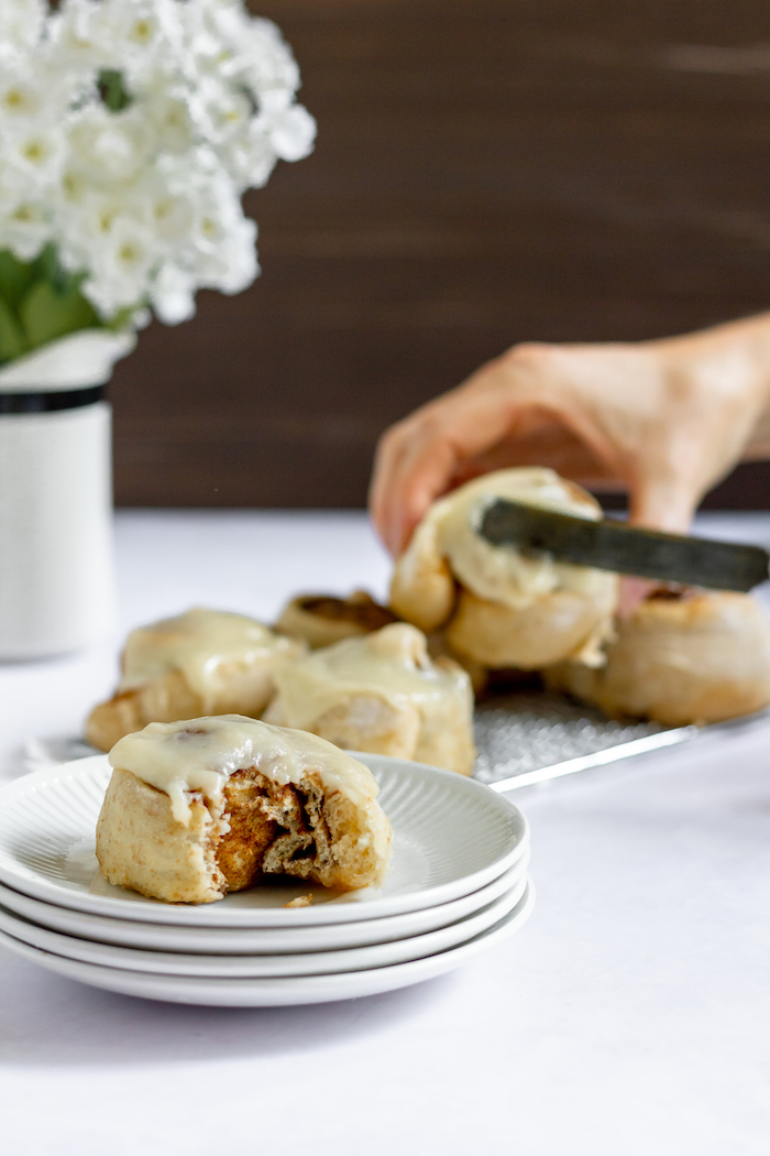 Photo shows a hand serving cinnamon rolls on a white table