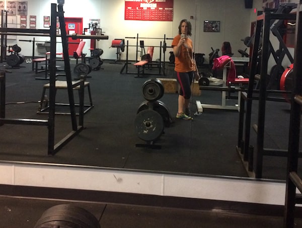 Image shows a woman standing in the weight room area of a gym