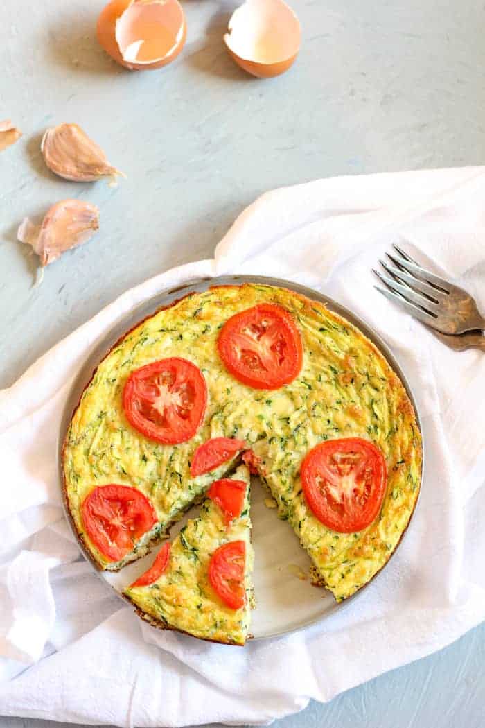 Image shows a dish of zucchini frittata on a white napkin next to a fork