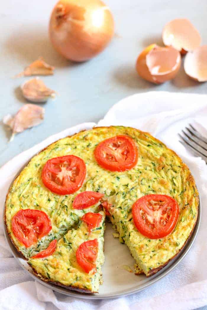 Image shows a pan of zucchini frittata next to several onions