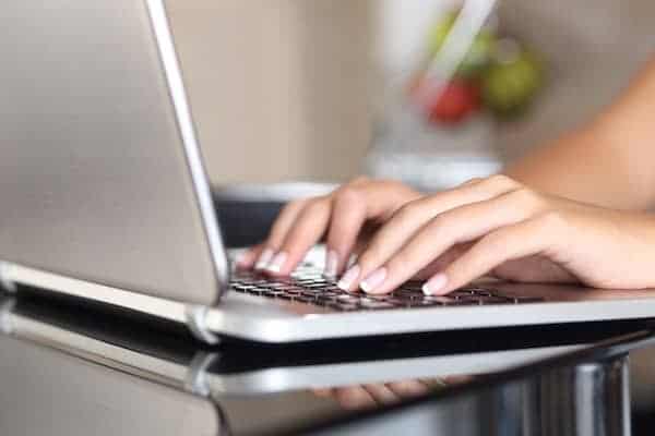 Image shows two hands typing on a laptop on a table