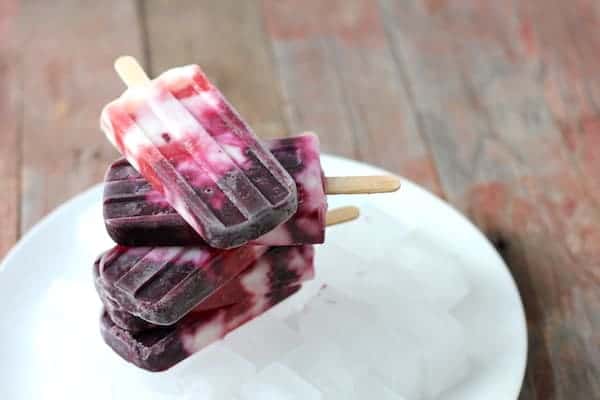 Image shows a white plate on a table, with several wild blueberry yogurt parfait popsicles stacked on the plate.