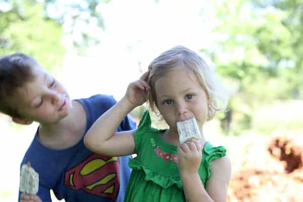 Image shows a young boy and girl eating breakfast popsicles outdoors