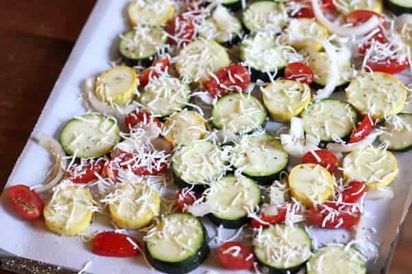 Image shows summer vegetables placed on a cookie sheet and topped with parmesan cheese
