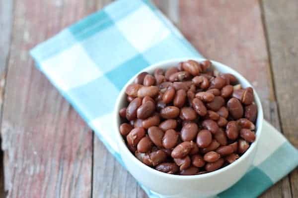 Image shows a bowl of cooked beans on a white and blue checkered napkin.