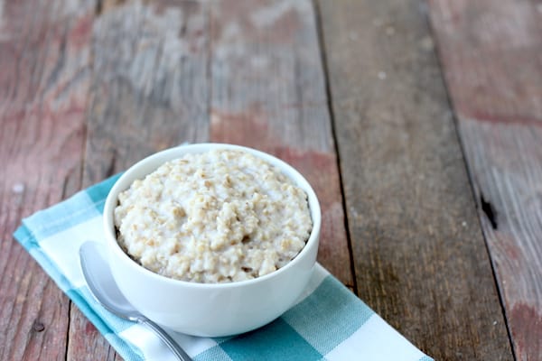 Image shows a white bowl sitting on a checkered napkin on a table, full of Instant Pot steel-cut oatmeal sprinkled in cinnamon.
