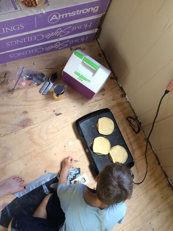 Photo, taken from above, shows a young boy making quesadillas on a small electric skillet on the floor of a room during renovation. 