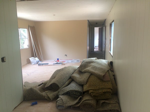 Image shows the interior of a mobile home with carpeting materials pulled up and piled on one side of the room.