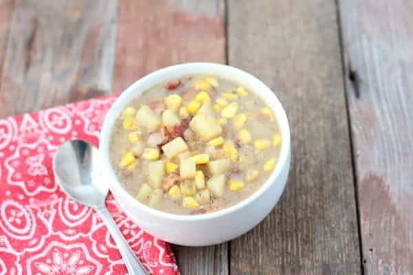 Photo shows a bowl of bacon and potato corn chowder on a table 