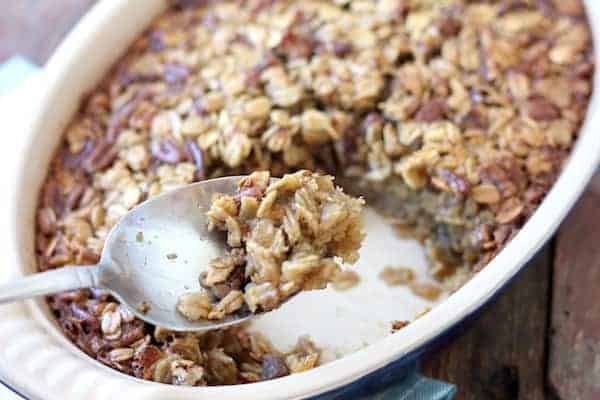 Image shows a spoon full of baked oatmeal pecan pie over the full dish