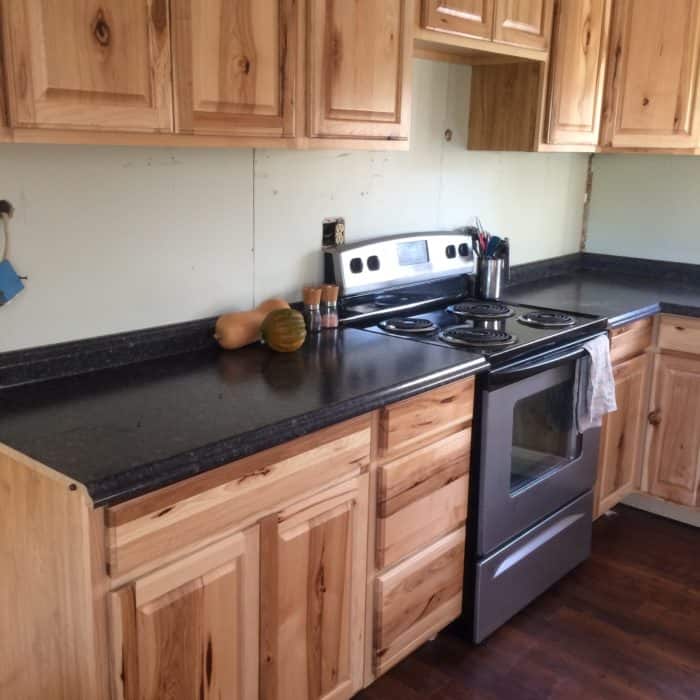 Photo shows a kitchen with dark counters and light wood cabinets