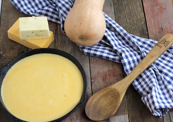 Image shows a pan of cheese sauce next to a towel and wooden spoon