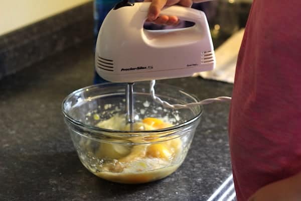 Image shows a hand mixer beating eggs in a glass bowl